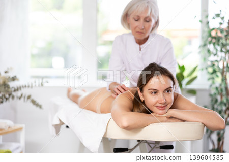 Young woman relaxing in spa center during professional back massage Young woman relaxing in spa center during professional back massage 139604585