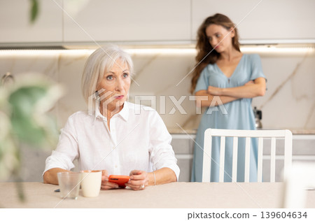 Adult woman quarreling with elderly woman in kitchen Adult woman quarreling with elderly woman in kitchen 139604634