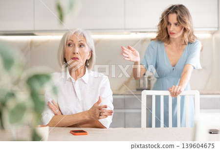 Adult woman quarreling with elderly woman in kitchen Adult woman quarreling with elderly woman in kitchen 139604675