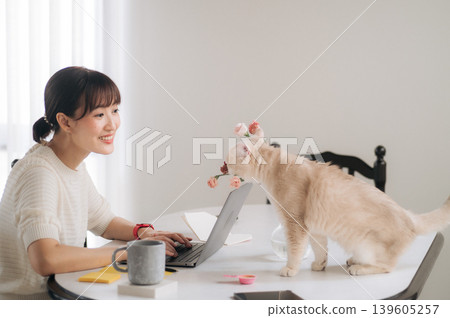 Happy asian woman enjoys laptop technology working alongside playful dog standing on table inside bright home office Happy asian woman enjoys laptop technology working alongside playful dog standing on table inside bright home office 139605257