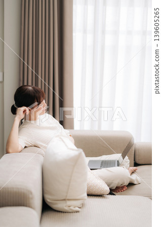 Peaceful asian woman sitting on comfortable sofa ignoring modern laptop technology feeling relaxed looking out bright window Peaceful asian woman sitting on comfortable sofa ignoring modern laptop technology feeling relaxed looking out bright window 139605265