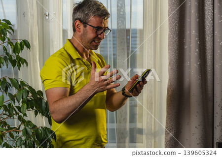 Emotional man reacting to online message near window Emotional man reacting to online message near window 139605324