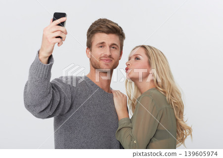 Selfie, happy and young couple in a studio for memory with love, care and sweet relationship. Smile, kiss and man and woman with picture photography for positive and good attitude by white background Selfie, happy and young couple in a studio for memory with love, care and sweet relationship. Smile, kiss and man and woman with picture photography for positive and good attitude by white background 139605974