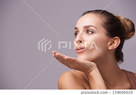 Skincare, kiss and young woman in a studio with health, wellness and dermatology routine. Cosmetic, confident and female person with natural facial treatment and flirt gesture by gray background. Skincare, kiss and young woman in a studio with health, wellness and dermatology routine. Cosmetic, confident and female person with natural facial treatment and flirt gesture by gray background. 139606020