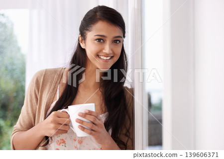 Coffee, happy and portrait of Indian woman by window for relaxing, comfortable and calm in home. Apartment, morning and person smile with mug drinking hot beverage, tea and caffeine in living room Coffee, happy and portrait of Indian woman by window for relaxing, comfortable and calm in home. Apartment, morning and person smile with mug drinking hot beverage, tea and caffeine in living room 139606371