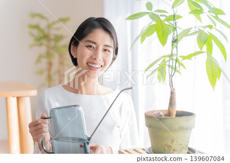 A woman watering houseplants with a watering can. A woman watering houseplants with a watering can. 139607084