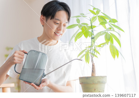一位年輕男子用澆水壺給盆栽植物澆水。 一位年輕男子用澆水壺給盆栽植物澆水。 139607117