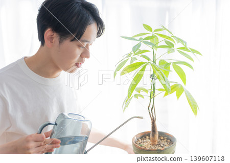 一位年輕男子用澆水壺給盆栽植物澆水。 一位年輕男子用澆水壺給盆栽植物澆水。 139607118