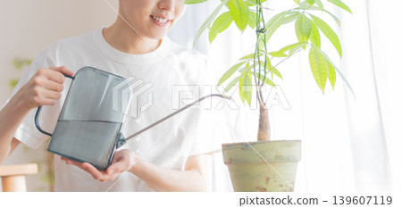 A young man waters a houseplant with a watering can. A young man waters a houseplant with a watering can. 139607119