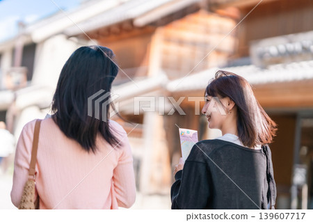 Two young women walking with the Kawagoe Toki no Kane (Time Bell) in the background. Girls' trip, strolling around town, sightseeing in Saitama. Two young women walking with the Kawagoe Toki no Kane (Time Bell) in the background. Girls' trip, strolling around town, sightseeing in Saitama. 139607717