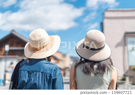 兩位年輕女子在擁有傳統倉庫的小鎮觀光;漫步街頭;暑假旅行照片。 兩位年輕女子在擁有傳統倉庫的小鎮觀光;漫步街頭;暑假旅行照片。 139607721