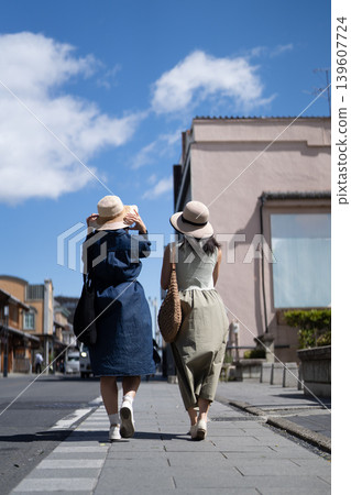 Two young women enjoying sightseeing in a town with traditional storehouses; strolling through the streets; summer vacation travel image. Two young women enjoying sightseeing in a town with traditional storehouses; strolling through the streets; summer vacation travel image. 139607724