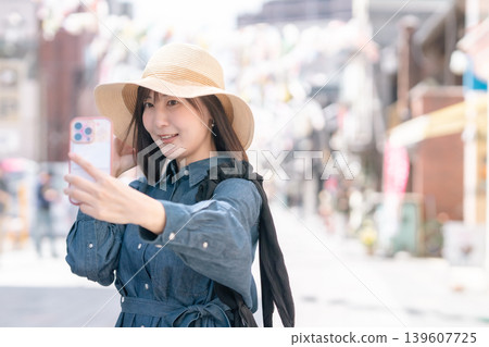 A young woman takes a selfie with her smartphone while sightseeing in Koedo Kawagoe. Travel destination, lifestyle, outing, holiday. A young woman takes a selfie with her smartphone while sightseeing in Koedo Kawagoe. Travel destination, lifestyle, outing, holiday. 139607725