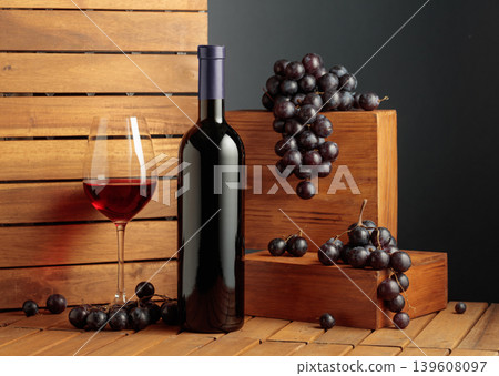 Bottle and glass of red wine and blue grapes on a wooden background. Bottle and glass of red wine and blue grapes on a wooden background. 139608097