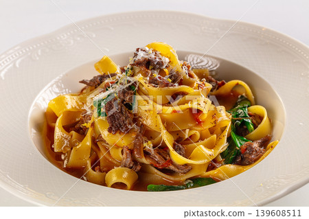 Gourmet fettuccine pasta with beef ragu and spinach, served in an ornate bowl on a white background 139608511