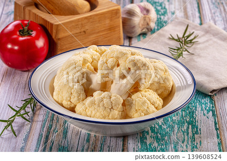 Fresh cauliflower florets in a bowl with tomato, garlic, and rosemary on a rustic wooden table 139608524