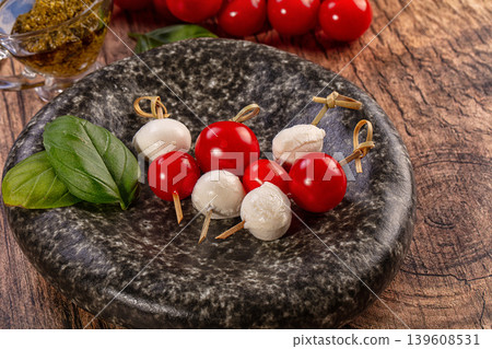 Caprese skewers with cherry tomatoes and mozzarella on a dark stone plate with basil and pesto Caprese skewers with cherry tomatoes and mozzarella on a dark stone plate with basil and pesto 139608531