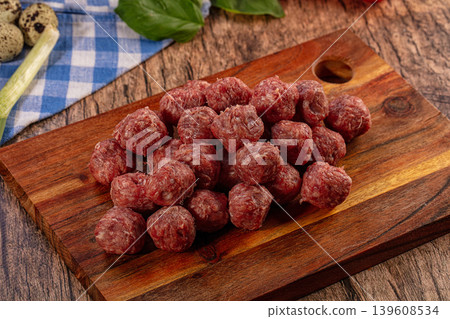 Raw homemade beef meatballs on a rustic wooden cutting board with fresh ingredients Raw homemade beef meatballs on a rustic wooden cutting board with fresh ingredients 139608534