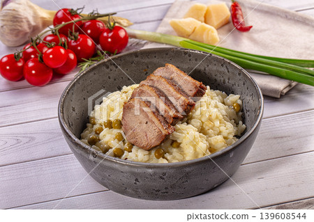 Creamy risotto with sliced meat, peas, parmesan cheese, cherry tomatoes, garlic, green onions, rustic wooden table Creamy risotto with sliced meat, peas, parmesan cheese, cherry tomatoes, garlic, green onions, rustic wooden table 139608544