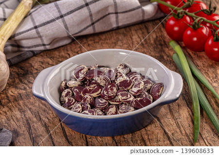 Raw pinto beans in ceramic bowl surrounded by fresh garlic, cherry tomatoes, and green onions on rustic wood 139608633