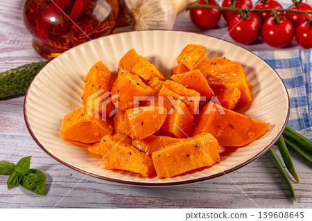 Roasted pumpkin cubes with herbs in ceramic plate surrounded by fresh vegetables on wooden table 139608645