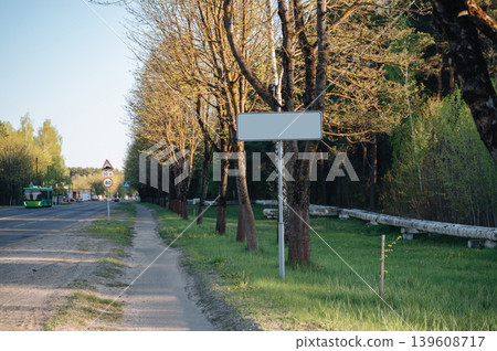 Empty asphalt road with a blank metal sign and a sidewalk lined with green trees and industrial pipes Empty asphalt road with a blank metal sign and a sidewalk lined with green trees and industrial pipes 139608717