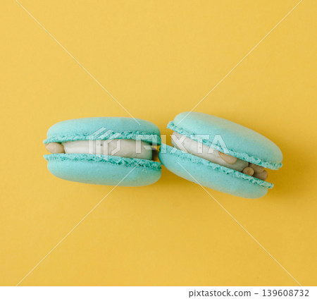 Two turquoise French macarons against a contrasting bright yellow background, vibrant color block dessert photography Two turquoise French macarons against a contrasting bright yellow background, vibrant color block dessert photography 139608732