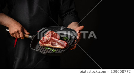 Chef holding raw porterhouse t bone steak in grill pan on dark background Chef holding raw porterhouse t bone steak in grill pan on dark background 139608772