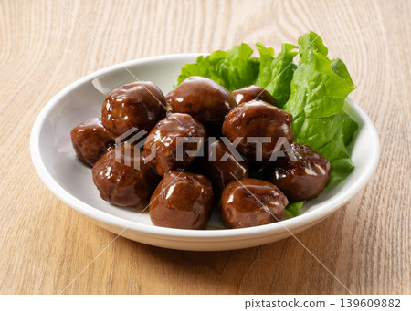 Meatballs served on a wood-grain table with teriyaki sauce and a side of lettuce. 139609882