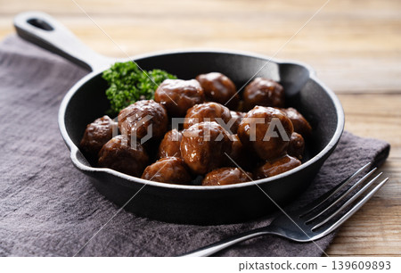 照燒肉丸盛於平底鍋中,佐以歐芹,置於木桌上,配上叉子。 照燒肉丸盛於平底鍋中,佐以歐芹,置於木桌上,配上叉子。 139609893