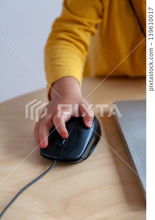 A hand of a child manipulates a laptop mouse, introducing concepts such as early access to social networks or teleworking. 139610017
