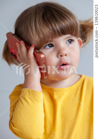 A toddler girl speaking on a smartphone, reflecting childhood interaction with modern devices. A toddler girl speaking on a smartphone, reflecting childhood interaction with modern devices. 139610023