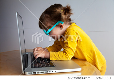 A small child typing and looking at a screen very close up, with the potential risks to eye health that come with exposure to electronic devices. 139610024