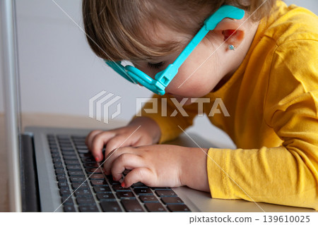 A toddler typing and looking very closed at a screen, with the potential risks to eye health that exposure to electronic devices entails. 139610025