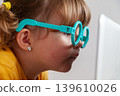 Small child with glasses exposed to blue light from a computer, introducing concepts such as the risk of developing eye diseases from accessing electronic devices at an early age. 139610026