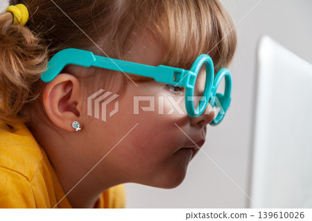 Small child with glasses exposed to blue light from a computer, introducing concepts such as the risk of developing eye diseases from accessing electronic devices at an early age. 139610026