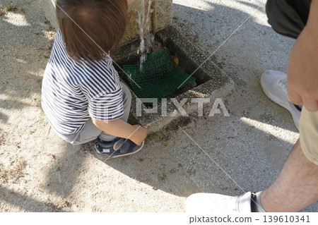 一個孩子和他的父親在公園的飲水噴泉旁玩水。 一個孩子和他的父親在公園的飲水噴泉旁玩水。 139610341