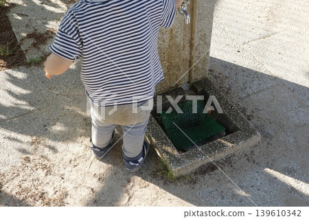 A child reaches for the tap at a drinking fountain in a park. A child reaches for the tap at a drinking fountain in a park. 139610342