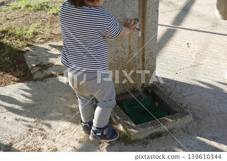 The back view of a child playing at a drinking fountain in a park. The back view of a child playing at a drinking fountain in a park. 139610344