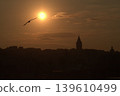 Galata Tower Sunset Silhouette with Soaring Bird. Iconic Istanbul landmark, Galata Tower, dramatically silhouetted against a fiery golden sunset. A bird flies toward the bright sun over the historic s 139610499