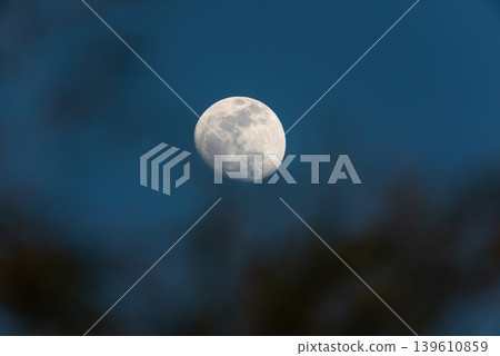 Detailed moon glowing in deep blue night sky with soft silhouette foreground creating peaceful astronomy and celestial atmosphere Detailed moon glowing in deep blue night sky with soft silhouette foreground creating peaceful astronomy and celestial atmosphere 139610859