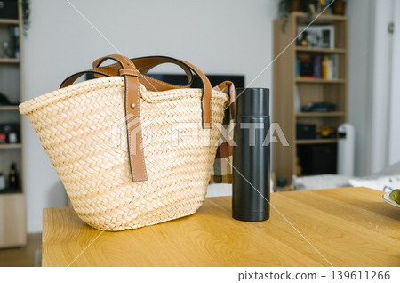Woven straw basket and black thermos on wooden table Woven straw basket and black thermos on wooden table 139611266