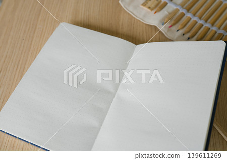 Open dotted notebook with colored pencils on wooden desk Open dotted notebook with colored pencils on wooden desk 139611269