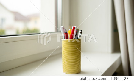 Yellow pen holder with assorted pens and pencils on windowsill Yellow pen holder with assorted pens and pencils on windowsill 139611271