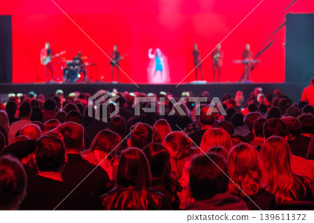 Crowd watching live music concert on stage with band and red lighting, audience enjoying show 139611372