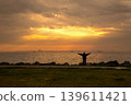 Sunrise silhouette fitness by the sea, rocky shoreline, golden sky reflections, serene morning exercise scene. 139611421