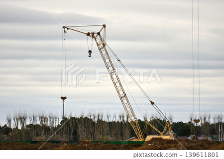 Giant tower crane over vacant building framework outdoors. Quiet city construction area featuring crane above vacant apartment framework Giant tower crane over vacant building framework outdoors. Quiet city construction area featuring crane above vacant apartment framework 139611801