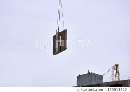 Industrial crane lifting a heavy concrete block for a residential building Industrial crane lifting a heavy concrete block for a residential building 139611812