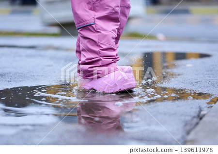 Pure childhood joy: little kid stomping in a puddle with flying water drops 139611978