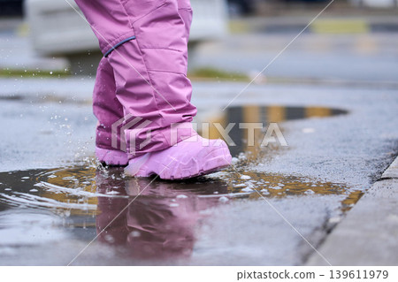 Childhood joy and outdoor fun: little child playing with water reflections after rain Childhood joy and outdoor fun: little child playing with water reflections after rain 139611979